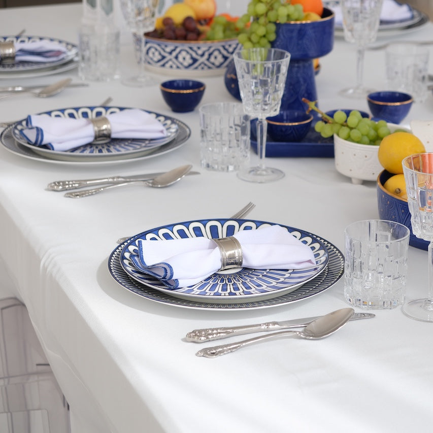 Qamar Bleu - Dinner Setup featuring a formal tablescape with blue-and-white china, silver flatware, stemmed glasses, decorative fruits, and metal lanterns for eight guests.