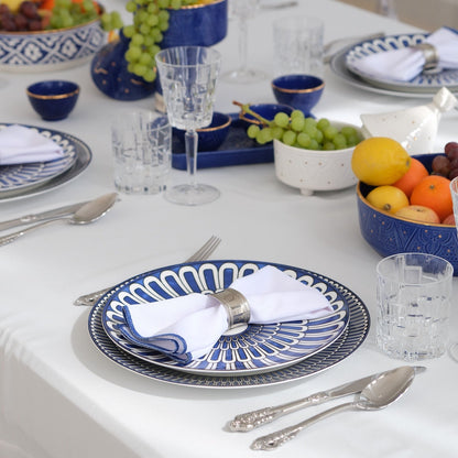 Qamar Bleu - Dinner Setup: A formal table for eight, featuring blue-and-white plates, silver napkin rings, crystal glassware, gold cutlery, fruit centerpieces, and elegant candle holders.