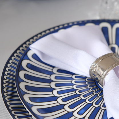Qamar Bleu - Dinner Setup showcases a detailed place setting with blue-and-white patterned plates, silver napkin ring, and blurred glass, perfect for elegant events.