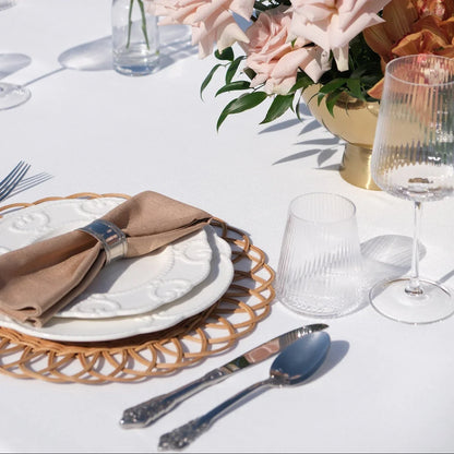 Luxe Alfresco - Dinner Setup featuring a table with rattan chargers, embossed china, gold cutlery, goblets, and blush rose centerpiece, perfect for elegant outdoor dining.