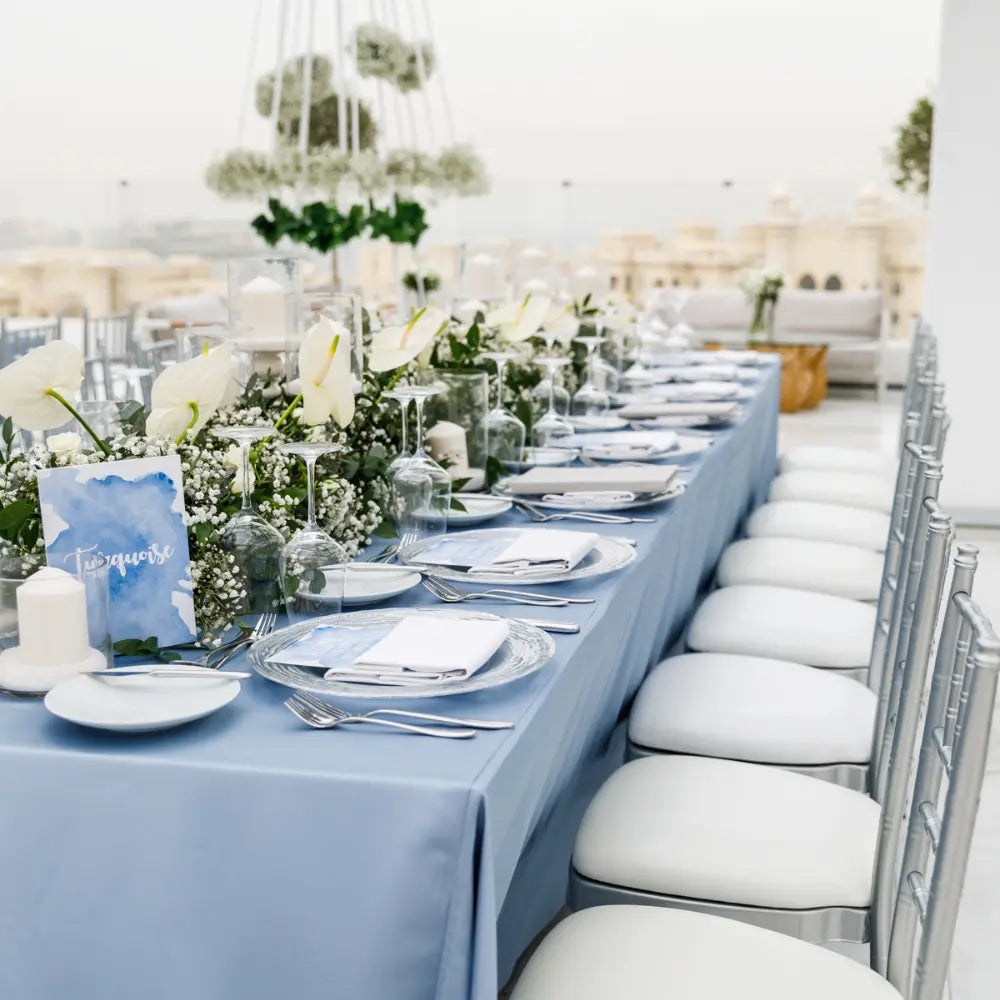Rectangular tablecloth satin drapes an elegant dining setup with greenery and white blooms, showcasing upscale event decor by Party Social.