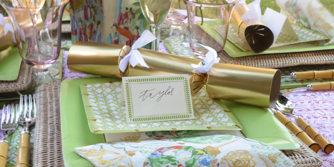 Decorative table setting with gold cracker, name card, and cutlery on a colorful tablecloth.