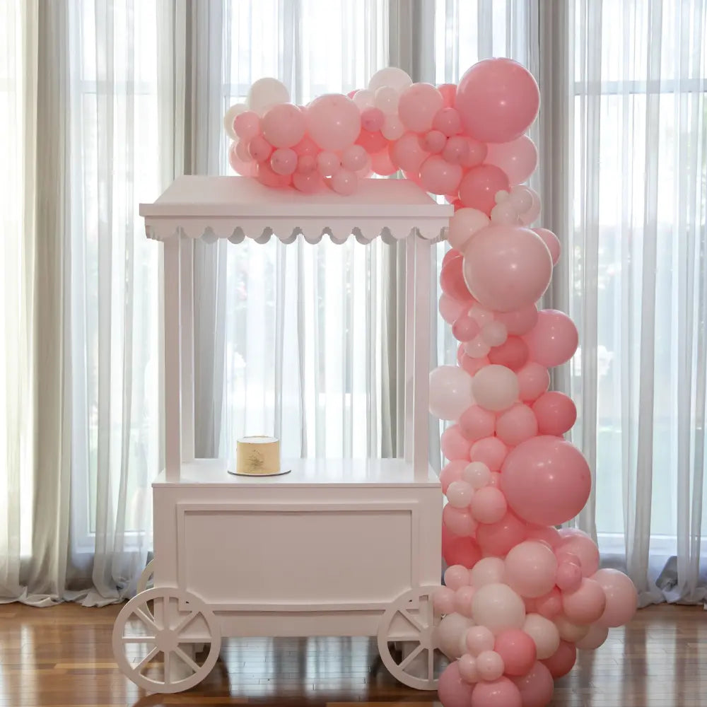 White Dessert Cart with balloon garland, showcasing a simple cake, ideal for parties or events as a stylish focal point.