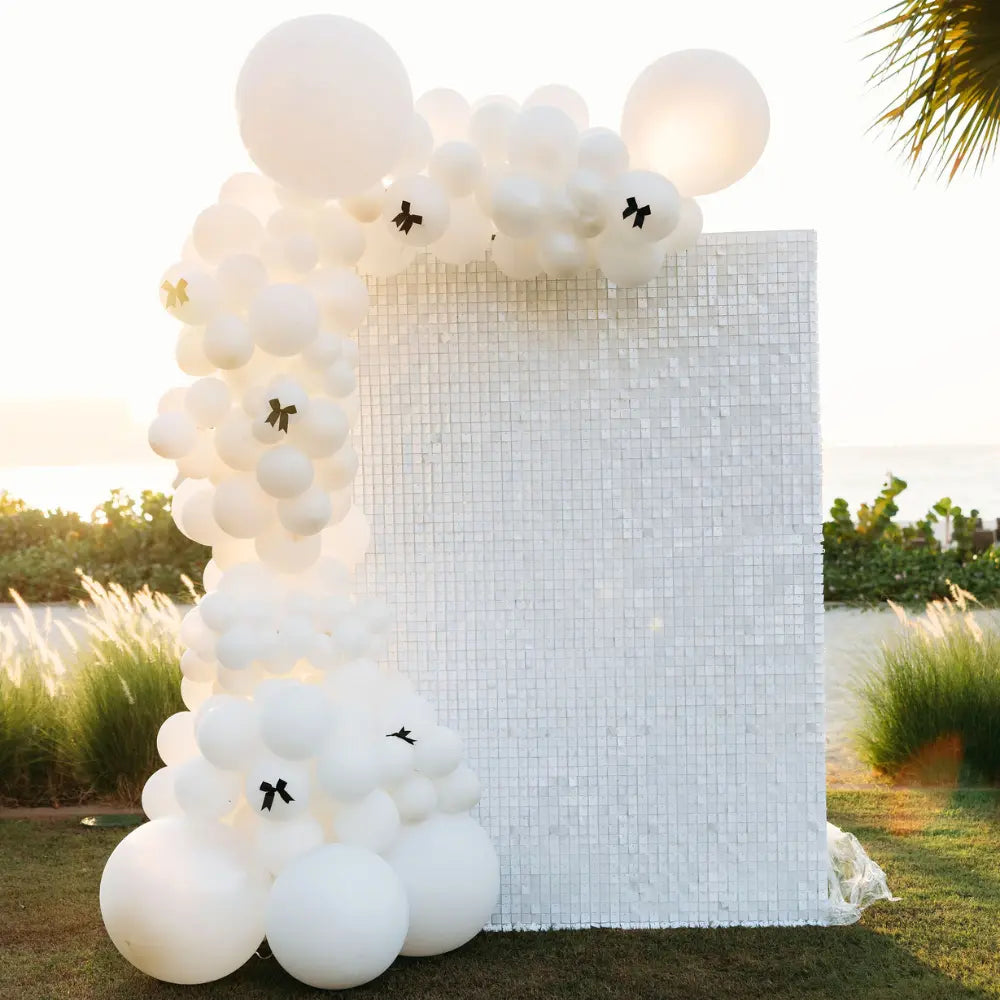 White balloon arch with decorative elements against a sequin wall backdrop. 
