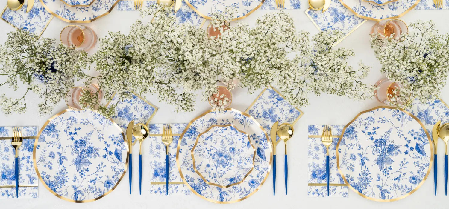 Decorative table setting with floral centerpieces, blue and white plates, and gold cutlery on a white background.