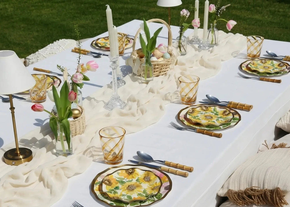 Elegant outdoor table setting with plates, glasses, and decorative elements on a white tablecloth.