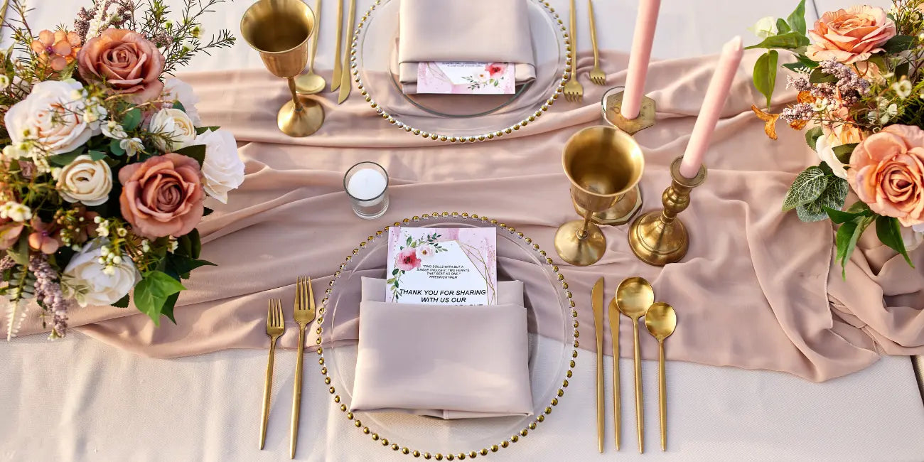 Elegant table setting with floral arrangements, gold cutlery, and pink napkins on a white tablecloth.
