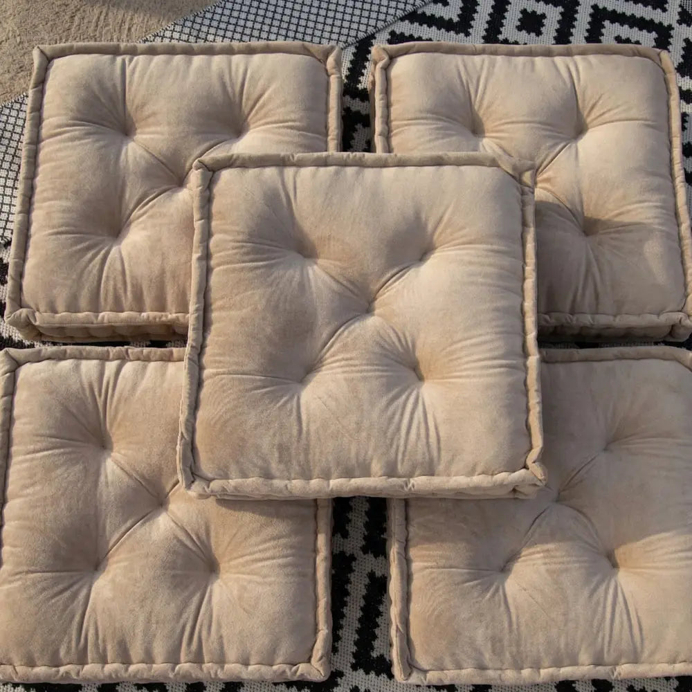FLOOR CUSHION VELVET: Five tufted, beige velvet floor cushions with piped edges, set on a black-and-white textile. Ideal for event seating or decor.