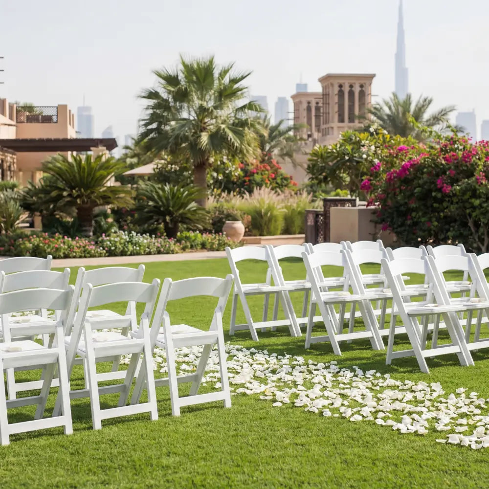 GARDEN CHAIR WHITE: Sleek white folding chairs set for an elegant outdoor event, enhancing the ambiance with their classic design amidst a lush, tropical backdrop.