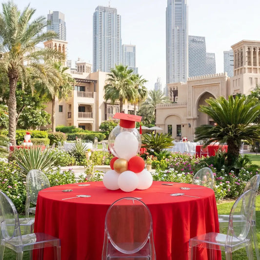 GHOST CHAIR W/O ARMS (VICTORIA) surrounds a table at a garden graduation event, showcasing clear, modern design amidst lush greenery and festive decor.