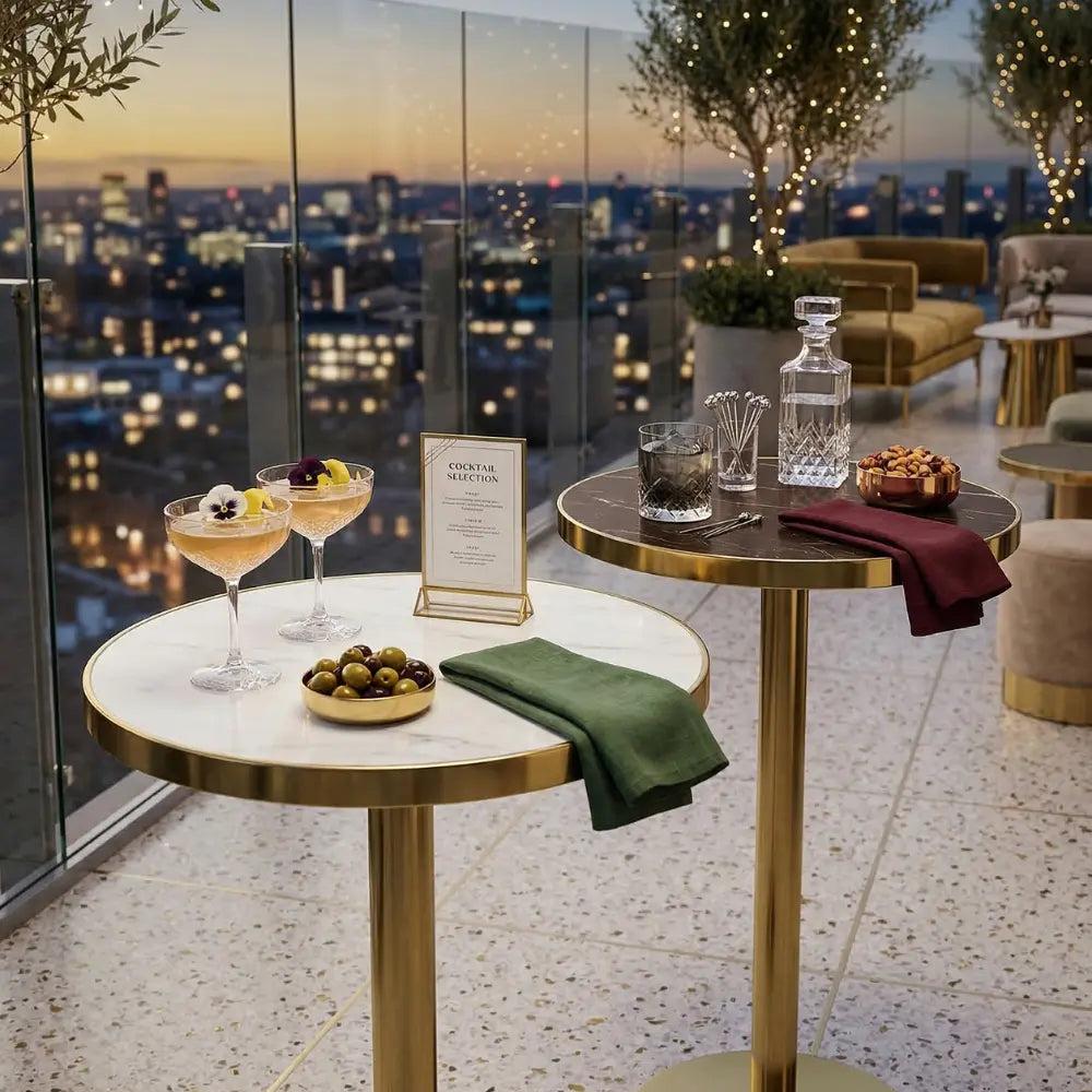 Gold Cocktail Tables with marble-look tops set with elegant glassware and snacks, overlooking a city skyline at dusk, ideal for stylish events.