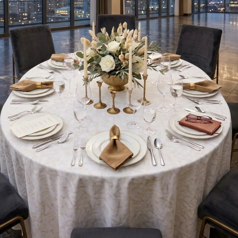 GOLD FOIL ROUND TABLECLOTH elegantly dresses a formal banquet table, featuring gold napkin rings, white roses, and gold candleholders, set for an upscale event.