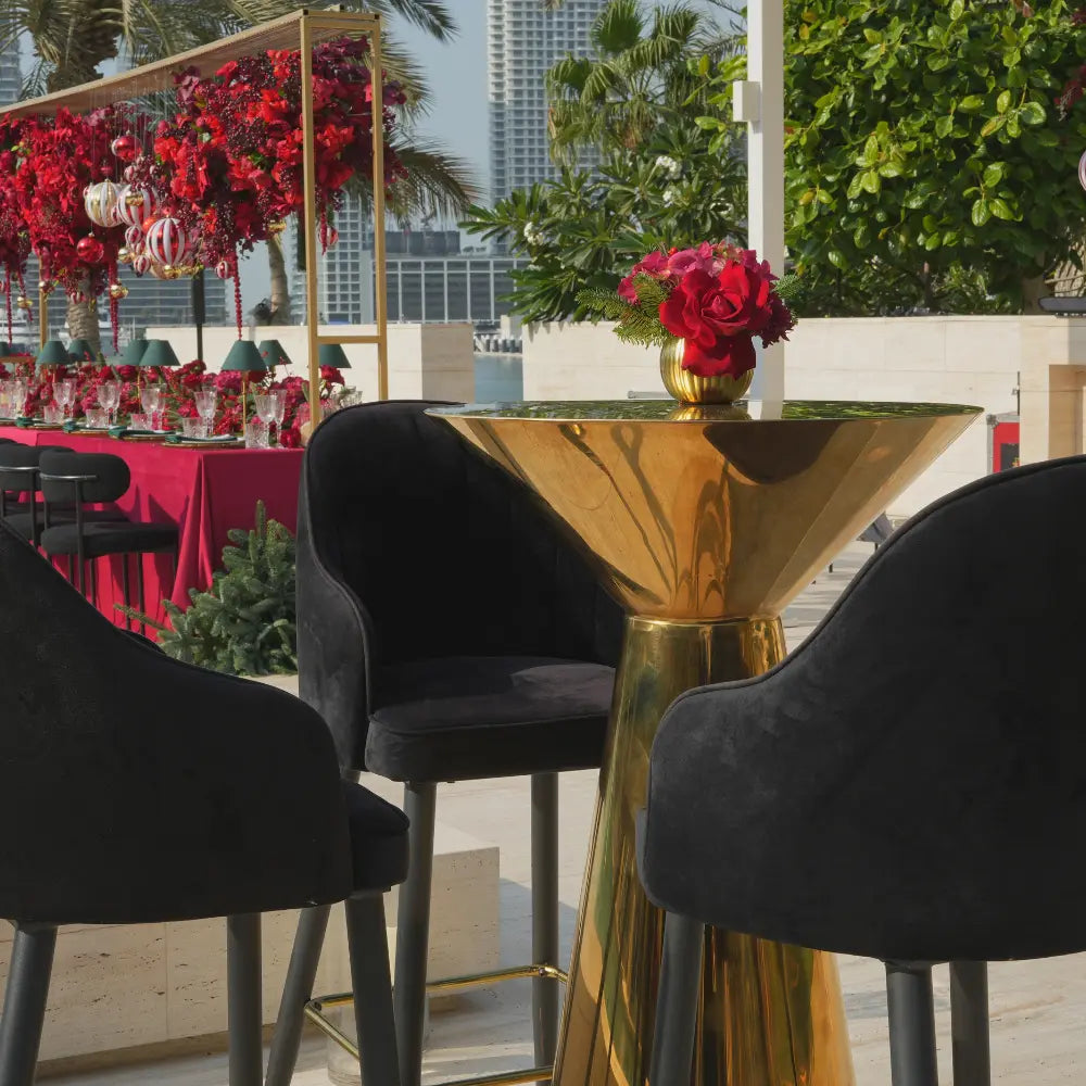 MIRROR COCKTAIL TABLES surrounded by black bar-height chairs in a festive setting, featuring a gold vase with red flowers, ideal for stylish events.