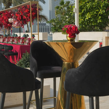 MIRROR COCKTAIL TABLES surrounded by black bar-height chairs in a festive setting, featuring a gold vase with red flowers, ideal for stylish events.