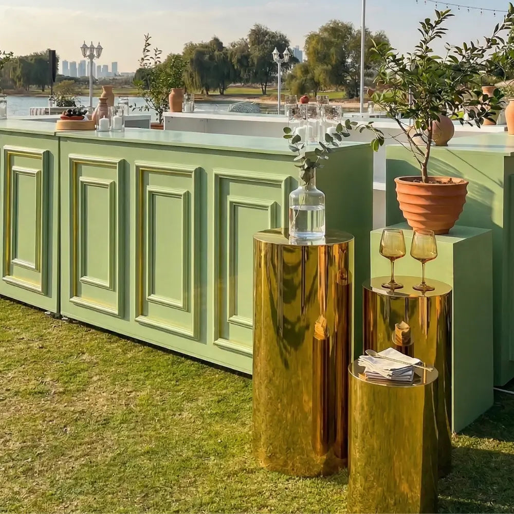 Gold Mirror Round Podium set on a lawn, showcasing a vase, wine goblets, and napkins, ideal for stylish outdoor events by Party Social.