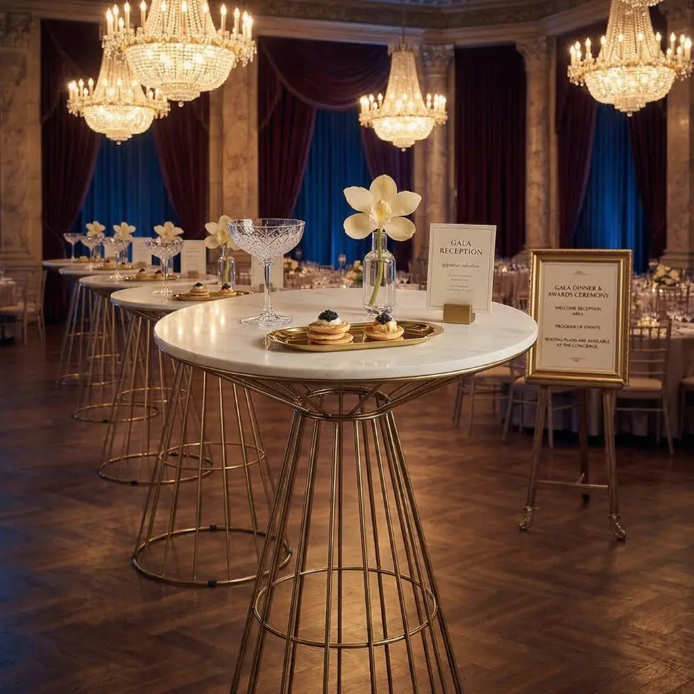 GOLD WIRE COCKTAIL TABLE - WHITE MARBLE TOP elegantly set for a gala with crystal glasses and hors d’oeuvres, under chandeliers in a luxurious ballroom.