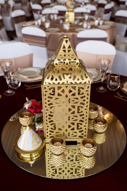 Gold Arabic Lantern with intricate patterns, displayed on a table. Ideal for event decoration. Candles not included. Various sizes available for rental or purchase.