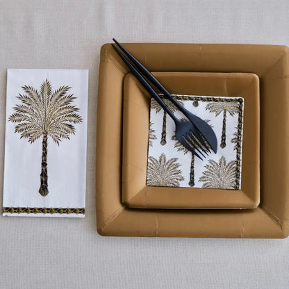 Brown square plate with black cutlery on a napkin with palm tree design, next to a matching napkin.