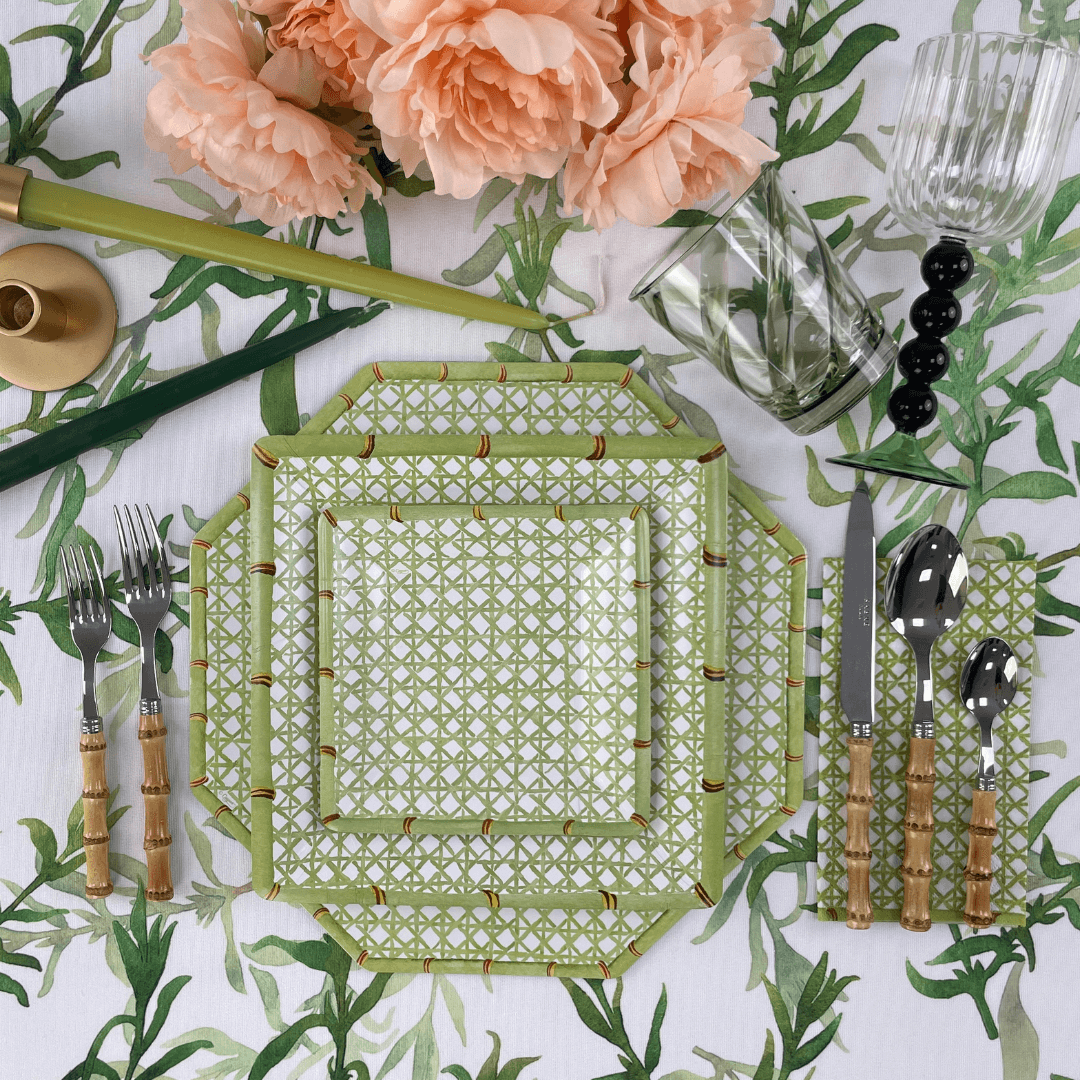 Holly Trellis Paper Dinner Plates - 8 Per Package displayed on a table with silverware and a glass vase with flowers.