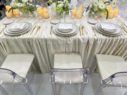 Classic Cream-Dining Setup featuring a banquet table with ivory-satin drape, gold-tone flatware, white floral centerpieces, and acrylic ghost chairs, perfect for elegant events.
