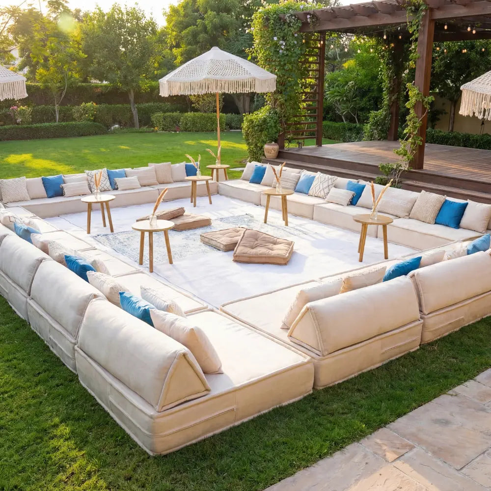 Lounge Low Seating arranged in a modular U-shape on a garden rug, adorned with throw pillows and cushions, under parasols and a vine-covered pergola.