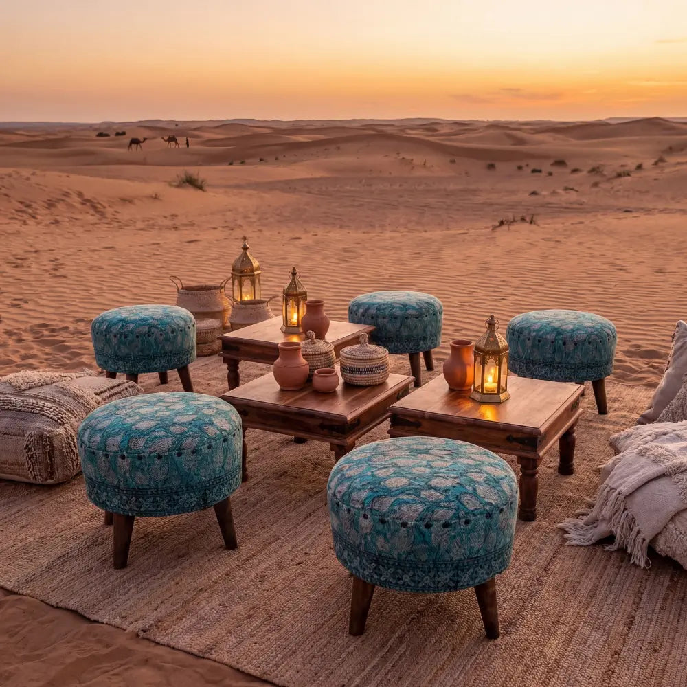 Low Stool with vintage-inspired textile and wooden legs, part of a desert lounge setup, surrounded by ottomans and lanterns on woven rugs at sunset.