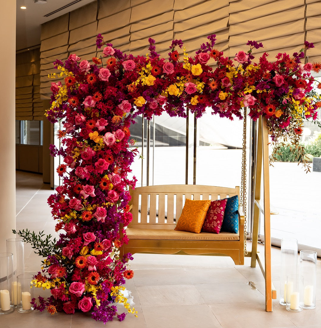 White Wooden Swing on a decorated bench with flowers and pillows, ideal for event props in parties or gatherings.