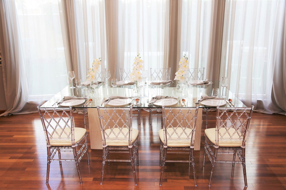 Glass dining table with clear top and white wooden bases, perfect for events and home functions, set for a dinner.