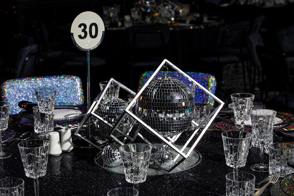 SILVER DUST ROUND CENTERPIECE elegantly displayed on a table, surrounded by glasses and a disco ball, enhancing dining setups with unique style.