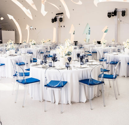 Round banquet tables set for an event, featuring clear plastic chairs with blue cushions, suitable for seating 6-8 guests in function halls.