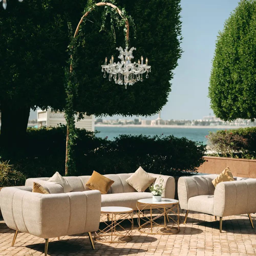 Lounge seating area with beige sofas, gold coffee table, and chandelier in a garden setting.
