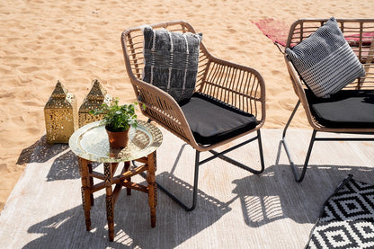 RATTAN COFFEE TABLE W/ GLASS TOP situated on a beach, accompanied by chairs, ideal for outdoor gatherings or events.