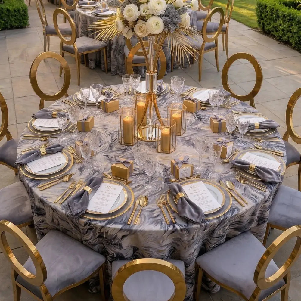 MODERN ABSTRACT PATTERN ROUND TABLECLOTH graces an outdoor dining setting, featuring gold-rimmed tableware, crystal glassware, and elegant gold accents, perfect for upscale events.