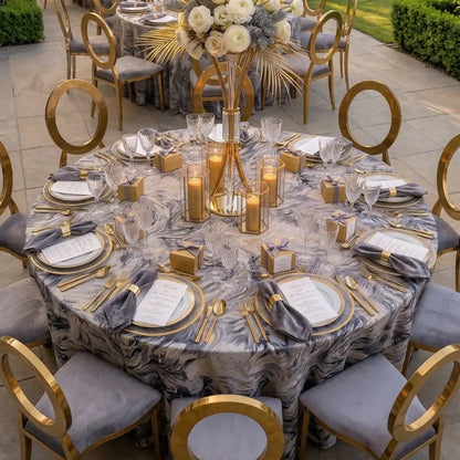 MODERN ABSTRACT PATTERN ROUND TABLECLOTH graces an outdoor dining setting, featuring gold-rimmed tableware, crystal glassware, and elegant gold accents, perfect for upscale events.