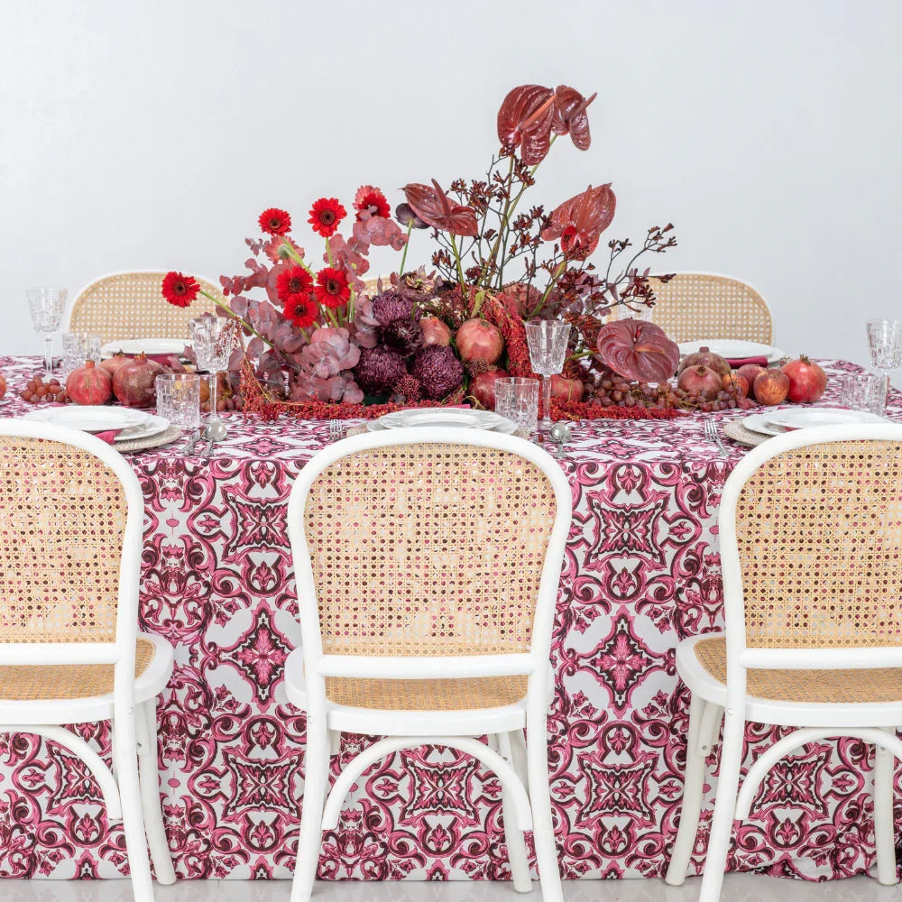 Decorative table setting with a floral centerpiece, patterned tablecloth, and wicker chairs.
