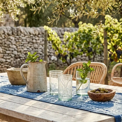 Outdoor setting with a table set for a meal, surrounded by greenery and stone wall.
