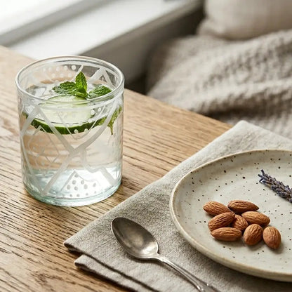 Glass of water with mint leaves, plate with almonds and lavender, and potted plant on a wooden table.