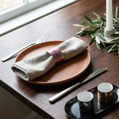 Dining table setting with plates, napkins, cups, and cutlery on a wooden surface.