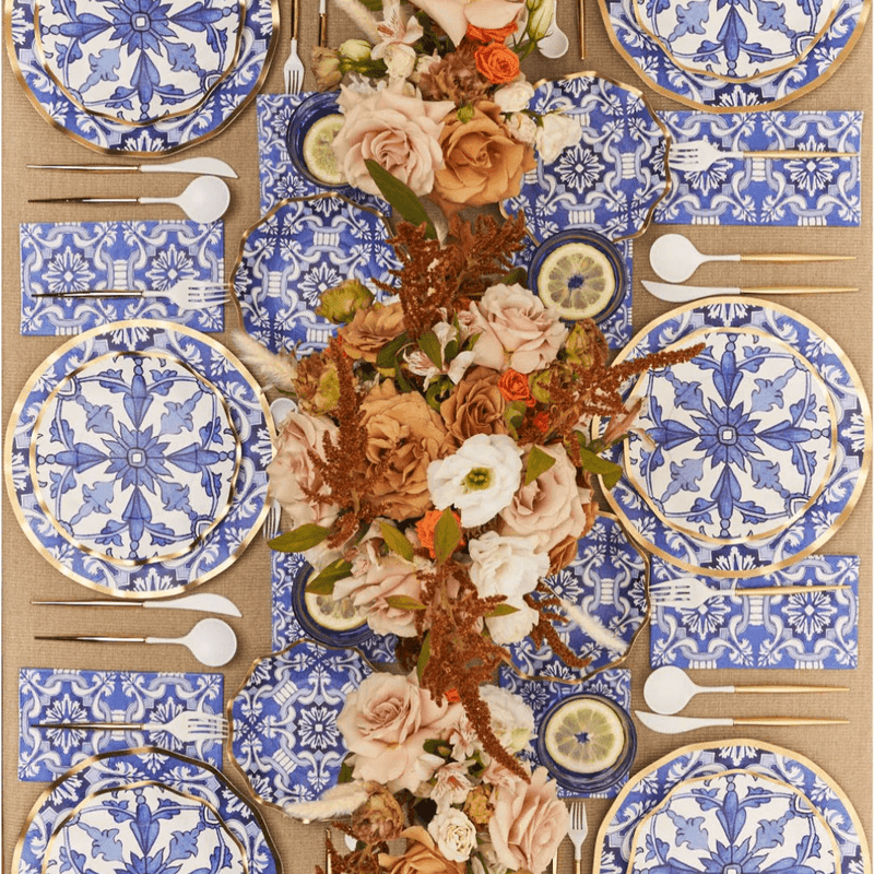 Blue tile pattern disposable party supplies with gold rim plates, matching napkins, and floral centrepiece.