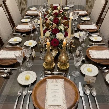 Dining table set with Arabesque polycotton napkins, wooden chargers, crystal stemware, silver flatware, menus, place cards, floral centerpiece, and candles for an elegant dinner party.