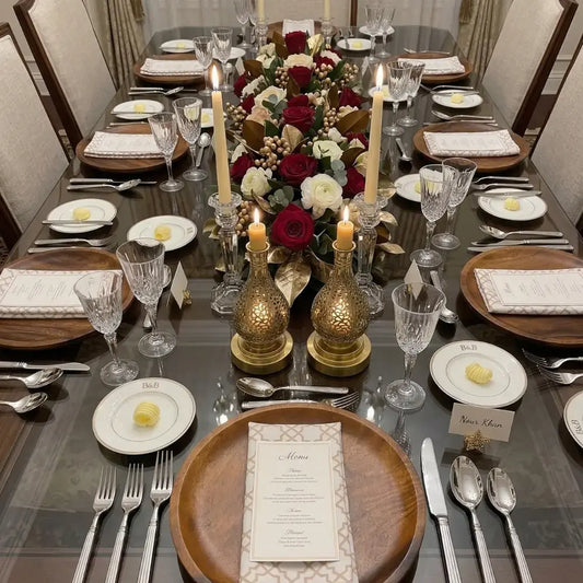 Dining table set with Arabesque polycotton napkins, wooden chargers, crystal stemware, silver flatware, menus, place cards, floral centerpiece, and candles for an elegant dinner party.