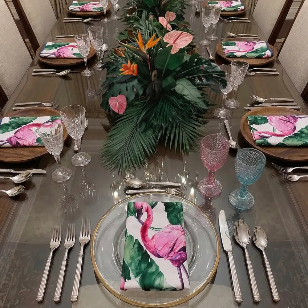 NAPKIN - FLAMINGO SATIN elegantly adorns the formal dining table, featuring vibrant flamingos and tropical leaves, complemented by crystal glasses and gold-rimmed chargers.