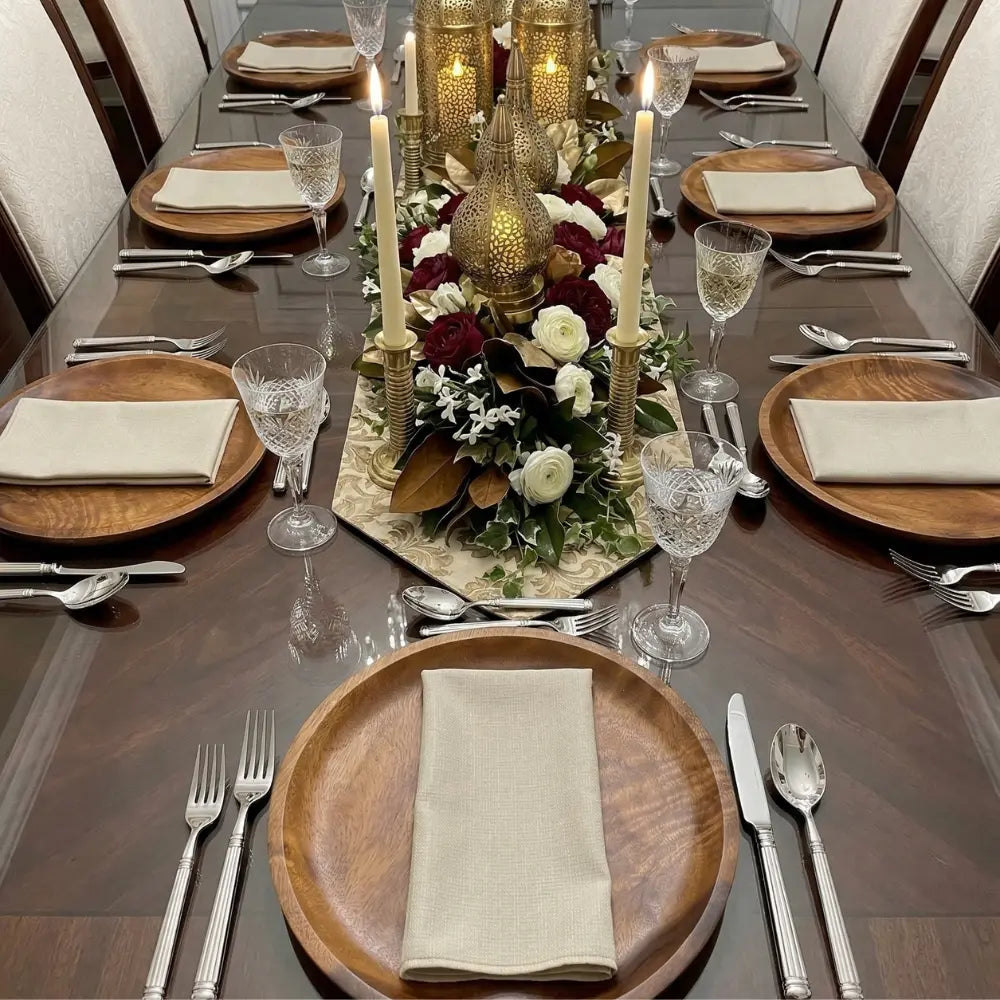 Elegant dining table with NAPKIN BLEACHED SAND W/ LINE, part of a formal setting with silver flatware, crystal goblets, and lush floral centerpiece.
