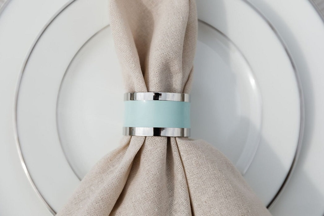 NAPKIN RING - SILVER &amp; AQUA ROUND on a plate, showcasing a simple, elegant design suitable for enhancing any tablescape.