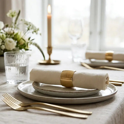 Elegant table setting with white plates, gold cutlery, and floral arrangements.