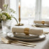 Elegant table setting with white plates, gold cutlery, and floral arrangements.