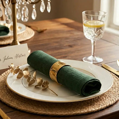 Elegant table setting with green napkins, gold cutlery, and a place card on a wooden table.