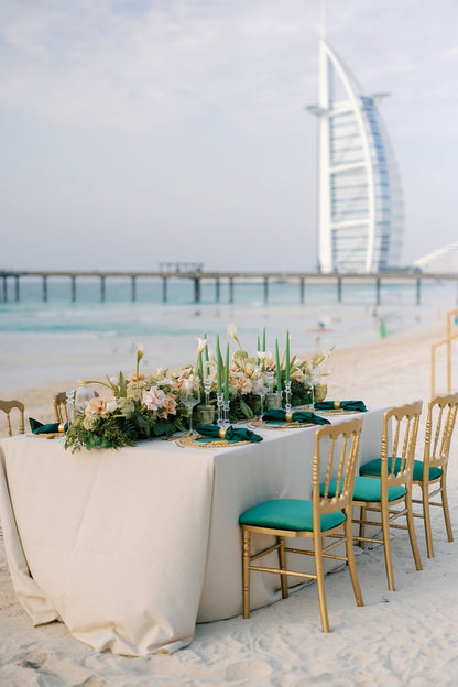 NAPOLEON GOLD CHAIR: An elegant armless chair set on a beach with a decorative table, ideal for weddings and events, highlighting versatility and style.