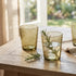 Green glass tumblers with water and herbs on a wooden table with a blurred garden background