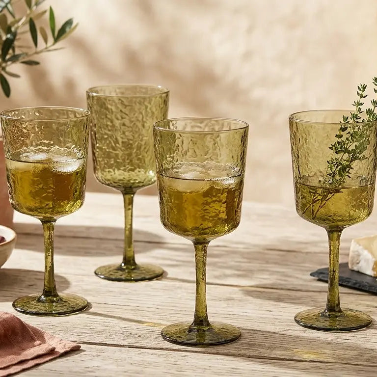 Set of green wine glasses on a wooden table with food and plants in the background